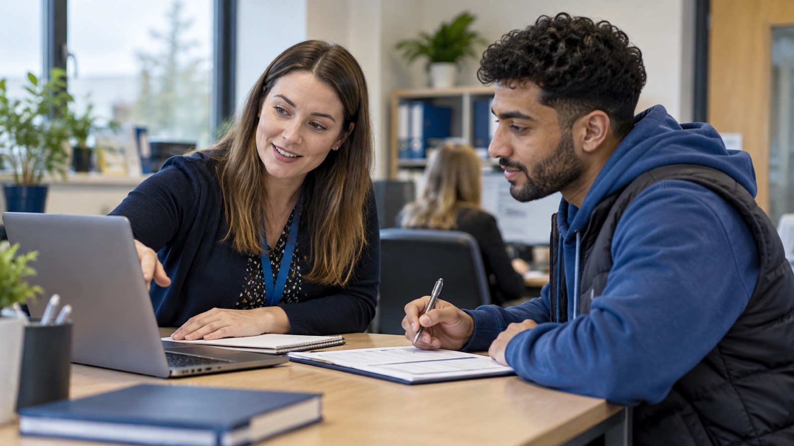 Training administrator guiding an adult learner through an enrolment form at a desk.